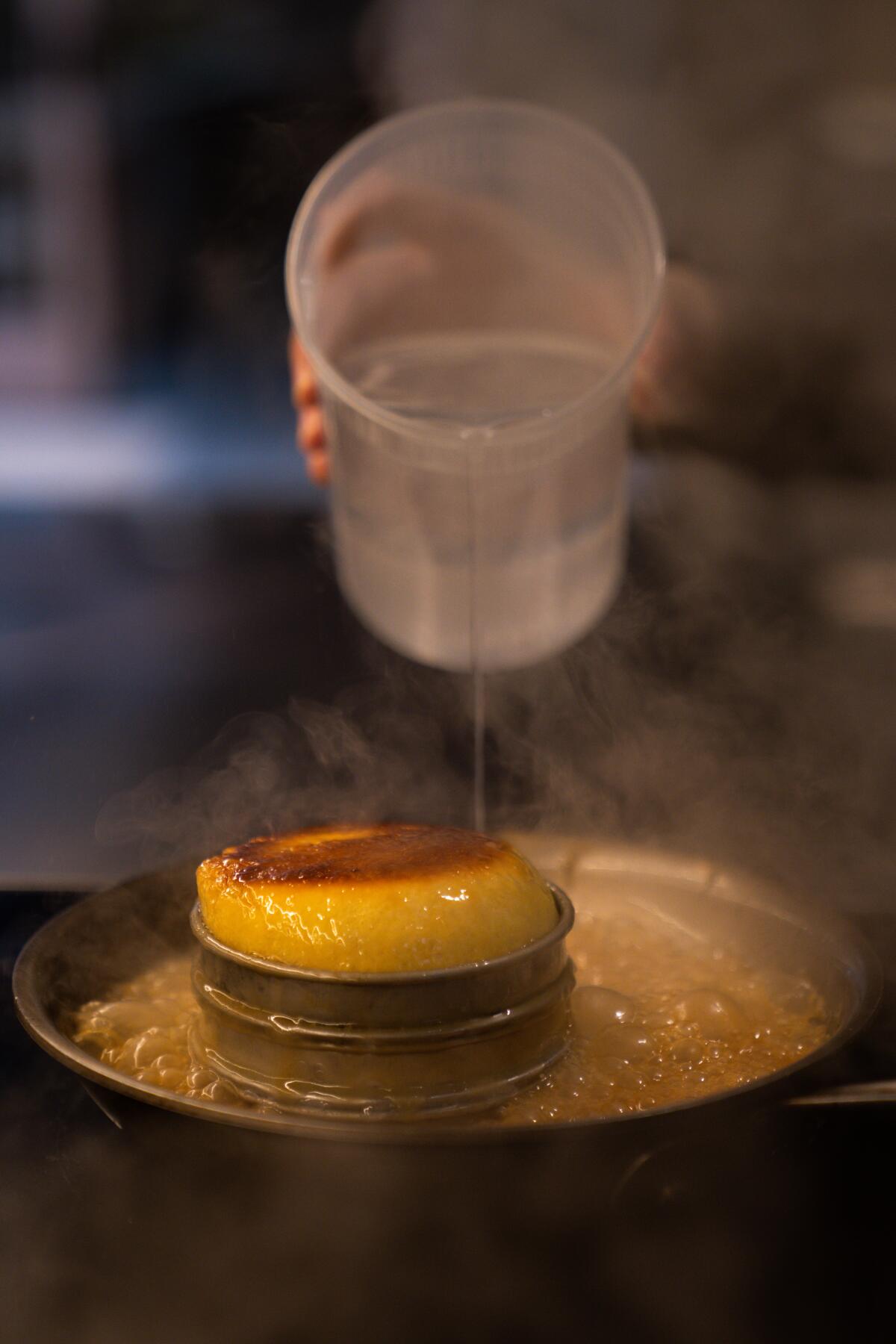 Water being poured from a plastic tub into a skillet with dough in a ring mold.