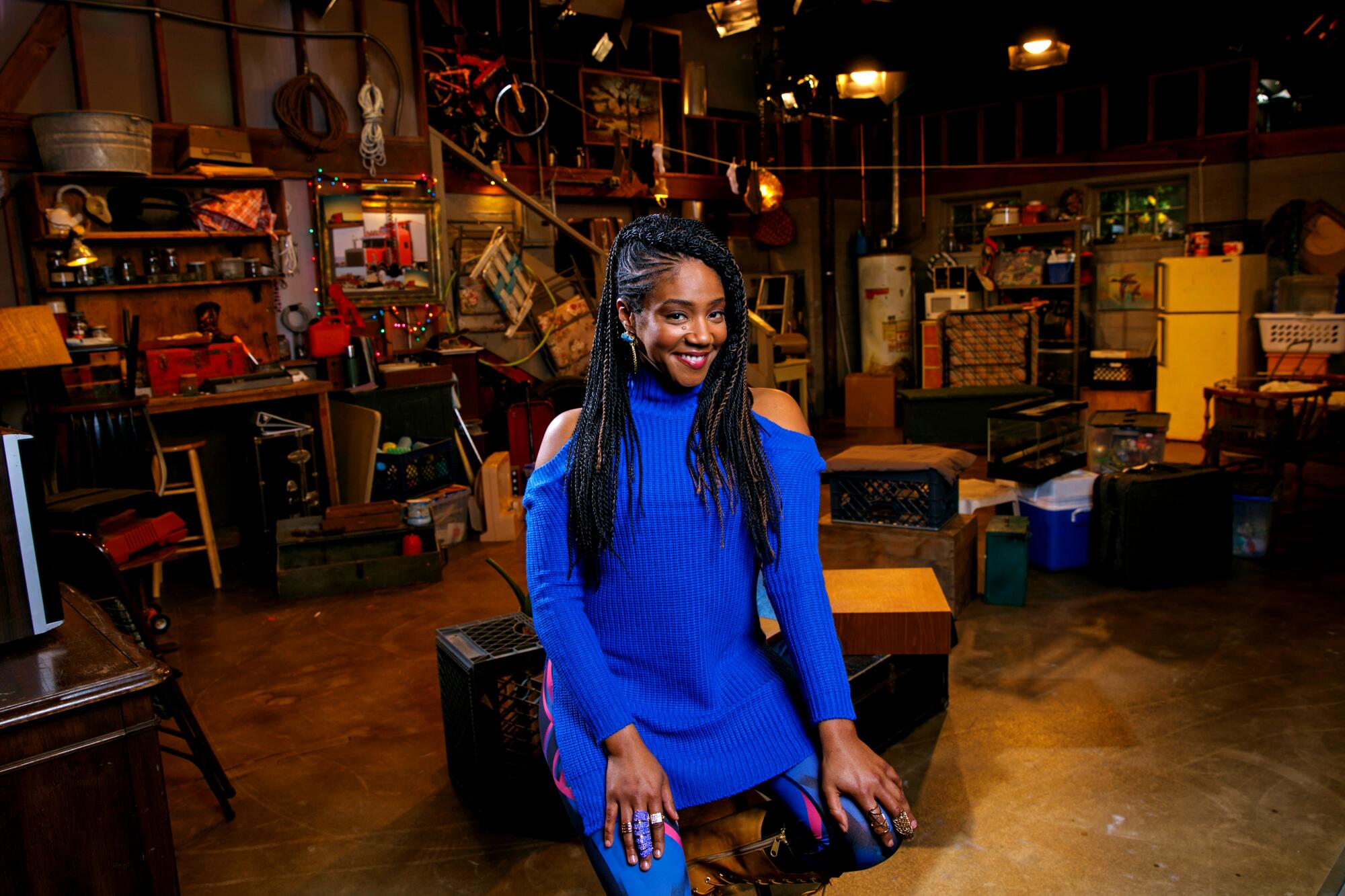 Actress Tiffany Haddish in a blue top with shoulder cutouts, on a TV set.