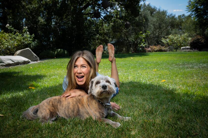 Jennifer Aniston lies on her stomach in the grass in her Los Angeles backyard, holding her dog Clyde.