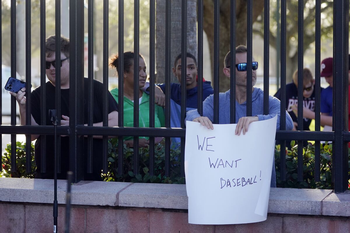 Baseball fans watch the commissioner speak and hold up a sign that reads "we want baseball."