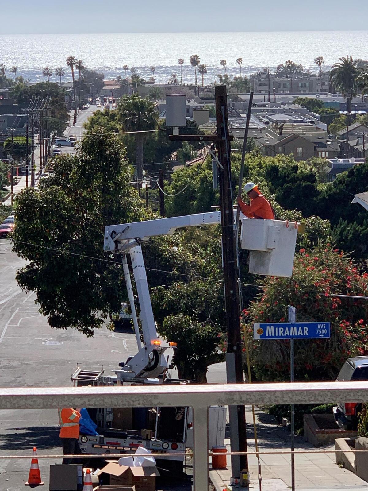 AT&T employees install a 5G miniature, cellular tower on a pole in front of La Jolla resident Harris Cohen’s house.