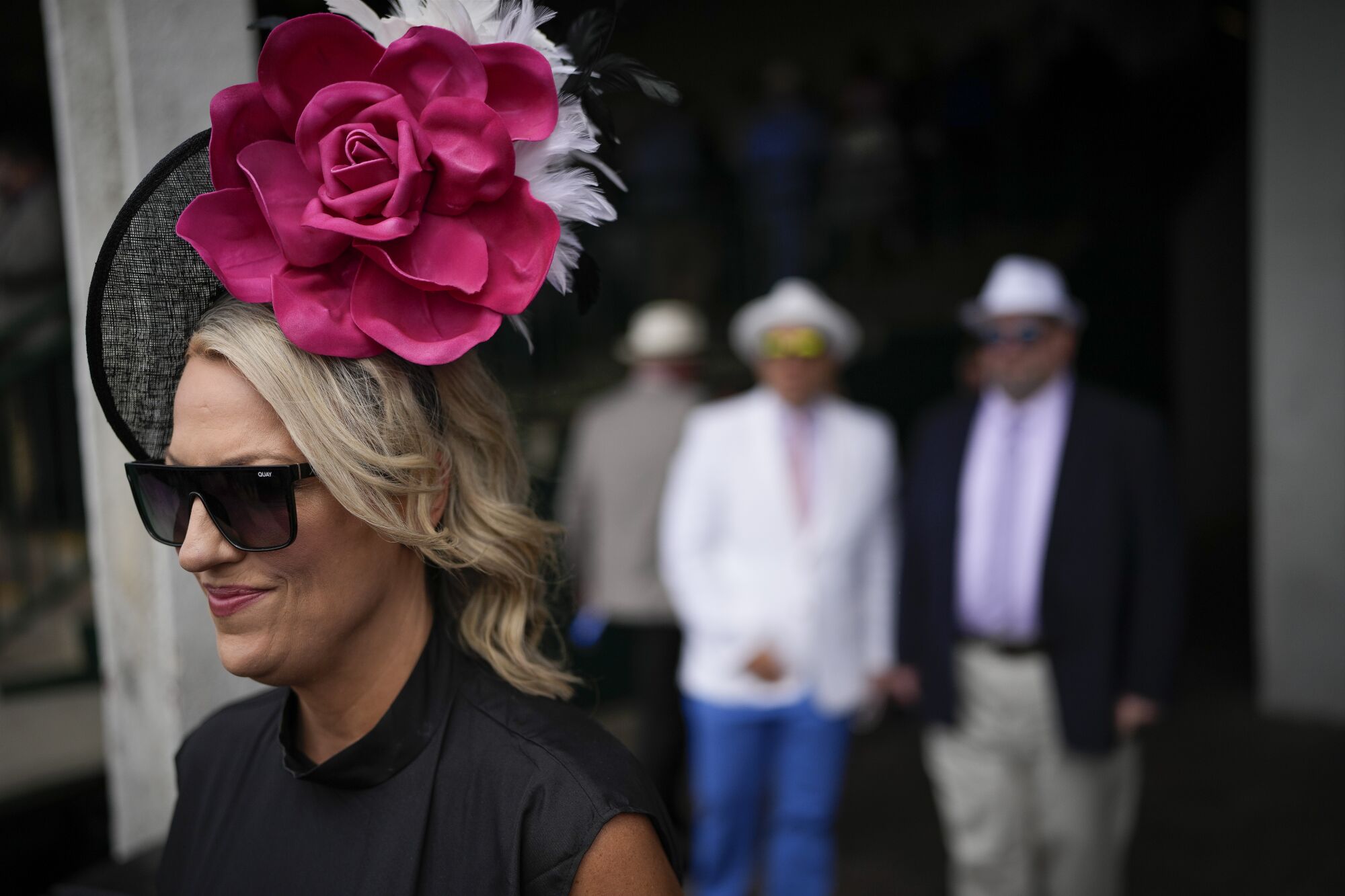 A woman wearing a hat with a large pink flower walks to her seat at Churchill Downs.