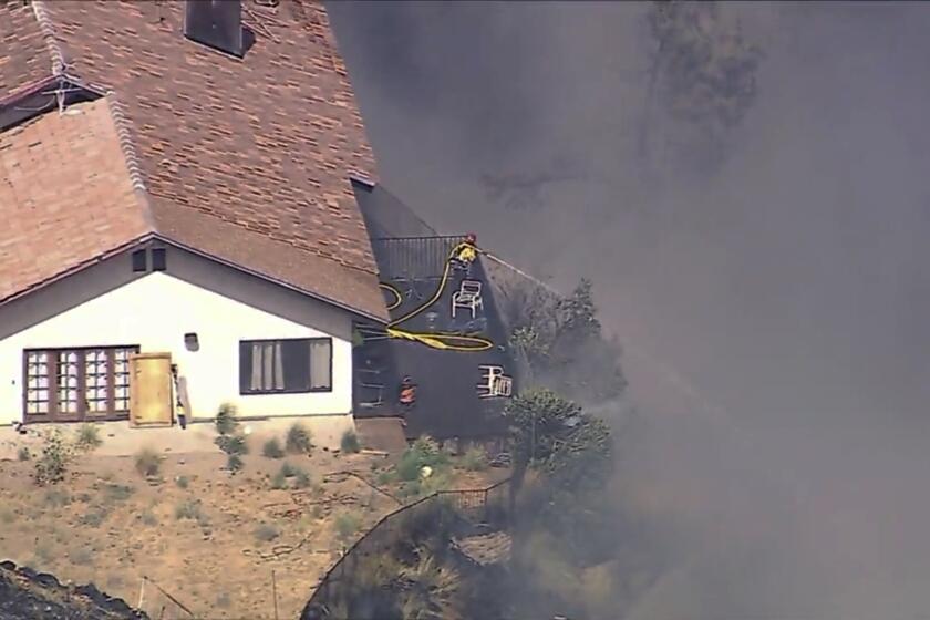 Un bombero rocía agua mientras varias casas se queman durante un incendio forestal en una comunidad ubicada en una ladera, en California, el lunes 5 de agosto 2024, en el condado de San Bernardino. (ABC7 Los Angeles vía AP)