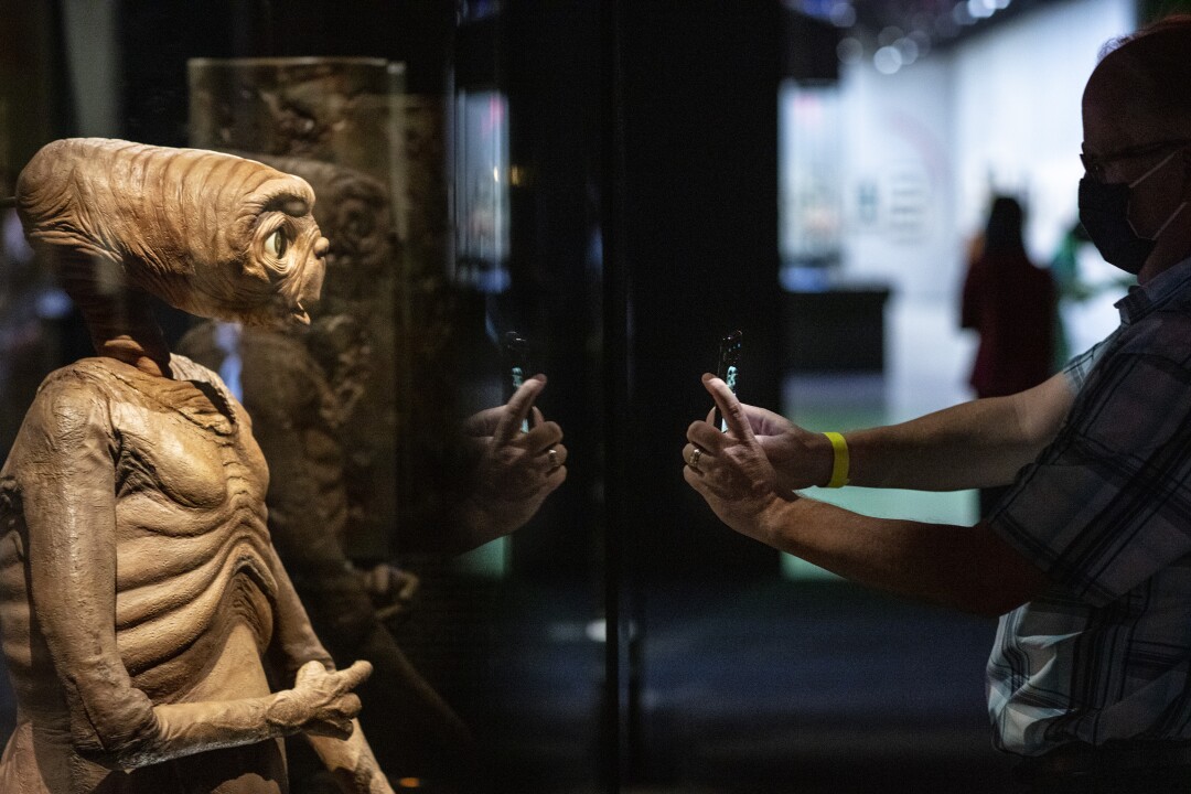 Una persona que sostiene un teléfono mete la mano en una caja de vidrio con ET "ET"