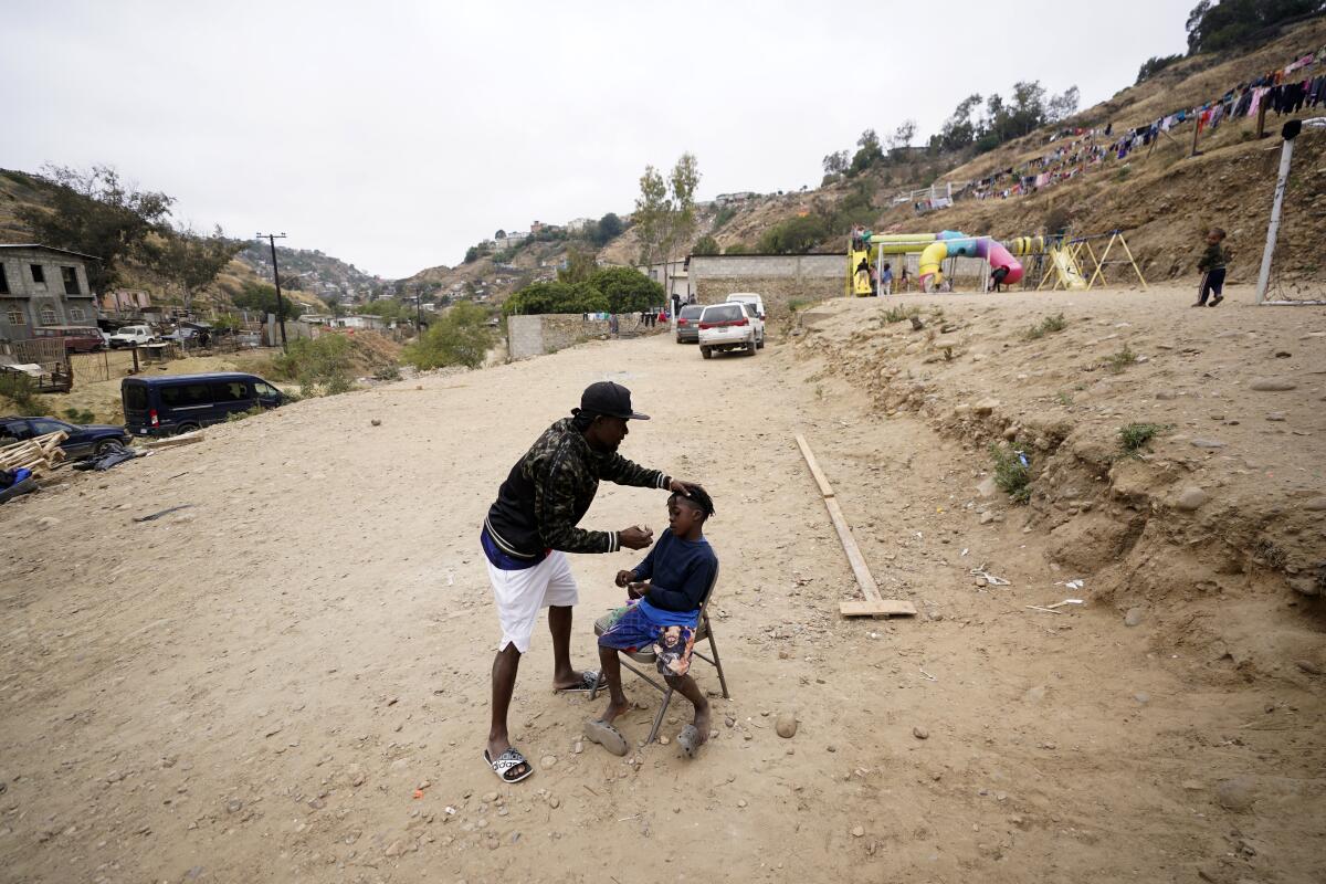 Wiggins Nordelus, of Haiti, cuts his son Samuel's hair outside of a shelter for migrants, May 23, 2022, in Tijuana, Mexico. 