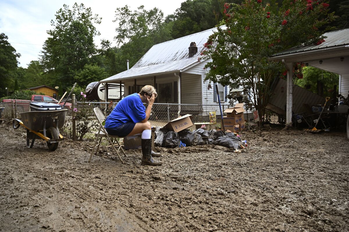 A woman sits with her head in her hands outside a flooded house.