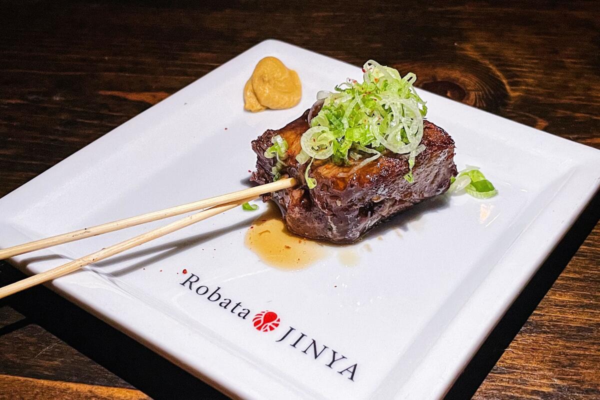 Beef tongue kushiyaki, skewered and topped with green onions, on a square plate with the words Robata Jinya