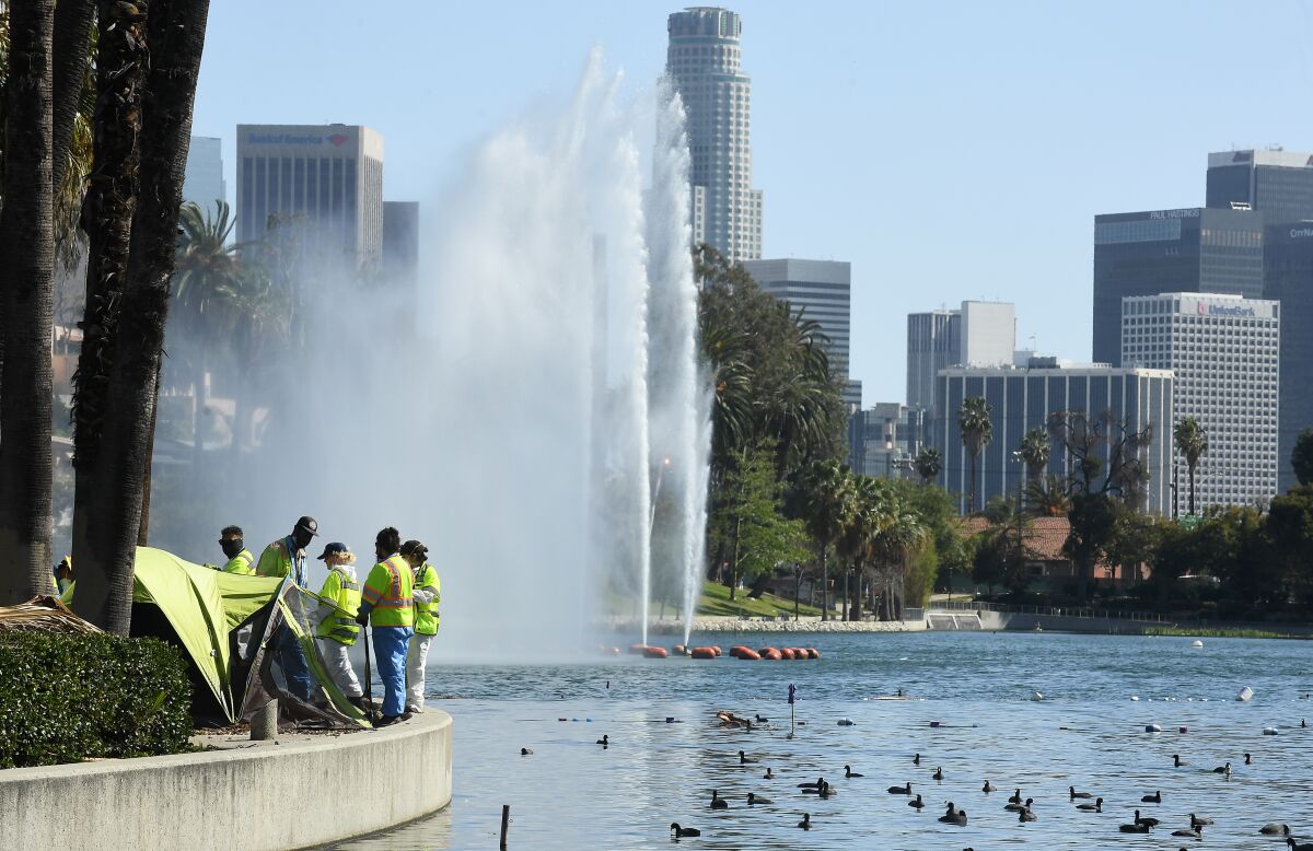 Work crews look over a tent next to Echo Park Lake, with the L.A. skyline in the background.