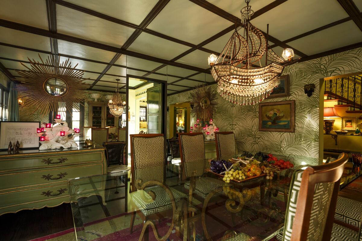 The dining room, which is furnished with French antiques, is punctuated with Christopher Hyland wallpaper in a palm frond motif, a Chinese Deco rug and a sparkling crystal ship chandelier from Z Gallerie.