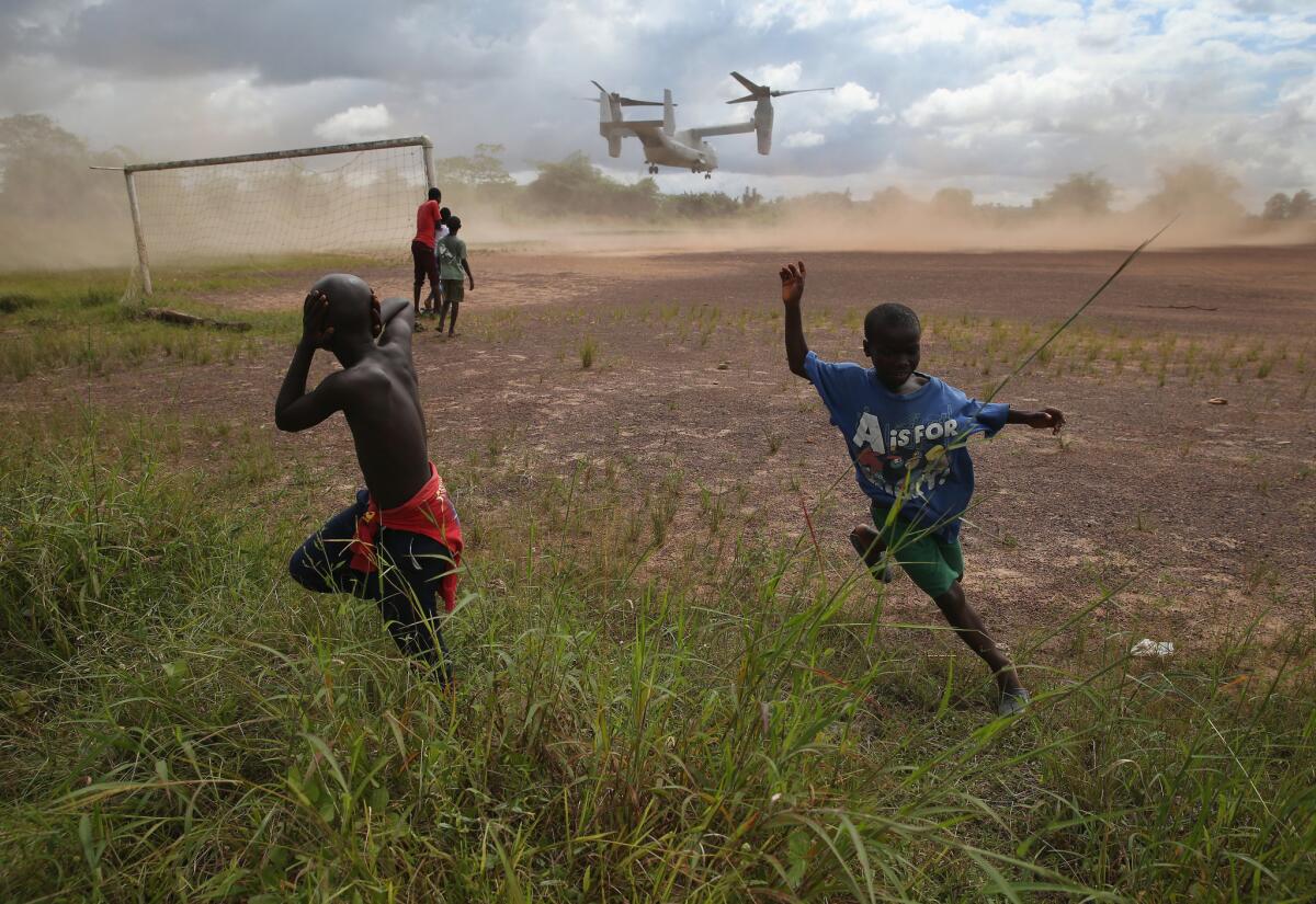 Boys run from the blowing dust as a U.S. aircraft departs the site of an Ebola treatment center under construction in Tubmanburg, Liberia, on Oct. 15. The center was the first of 17 built by Liberian forces under U.S. supervision.