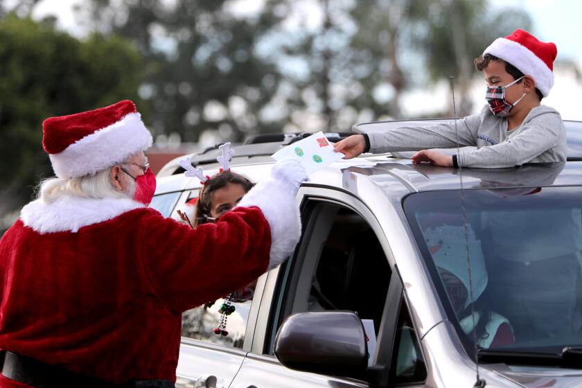 Santa Claus (Lou Martinez), left, gets a personalized letter from six-tear old Joey Martinez as his twin sister Elyse looks on, during the St. Bonaventure Catholic School Santa Drive-Thru Experience, at the campus in Huntington Beach on Saturday, Dec. 5, 2020.. Some children also brought letters for Santa, which he dropped into his giant mailbox.