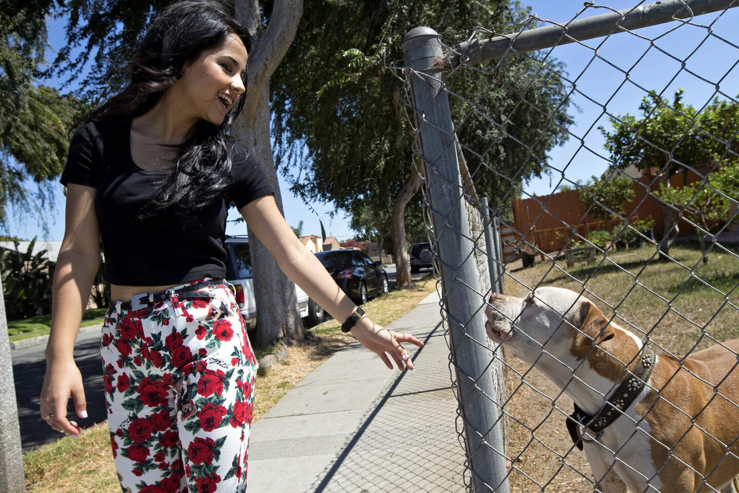 Rebbeca Marie Gomez, 16, a.k.a. Becky G, is greeted by a neighborhood dog as she walks along Oak Street in Inglewood.