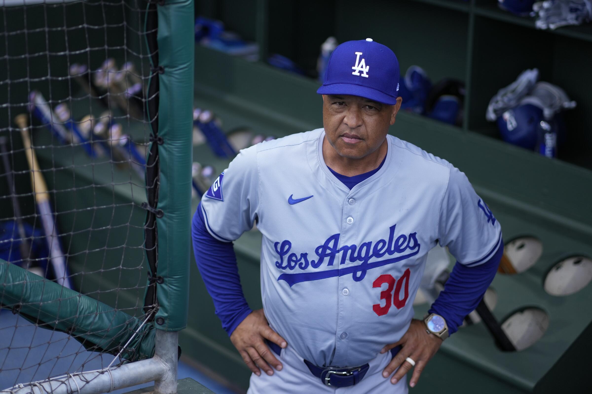 Dodgers manager Dave Roberts stands in the dugout with his hands on his hips as he watches a game.