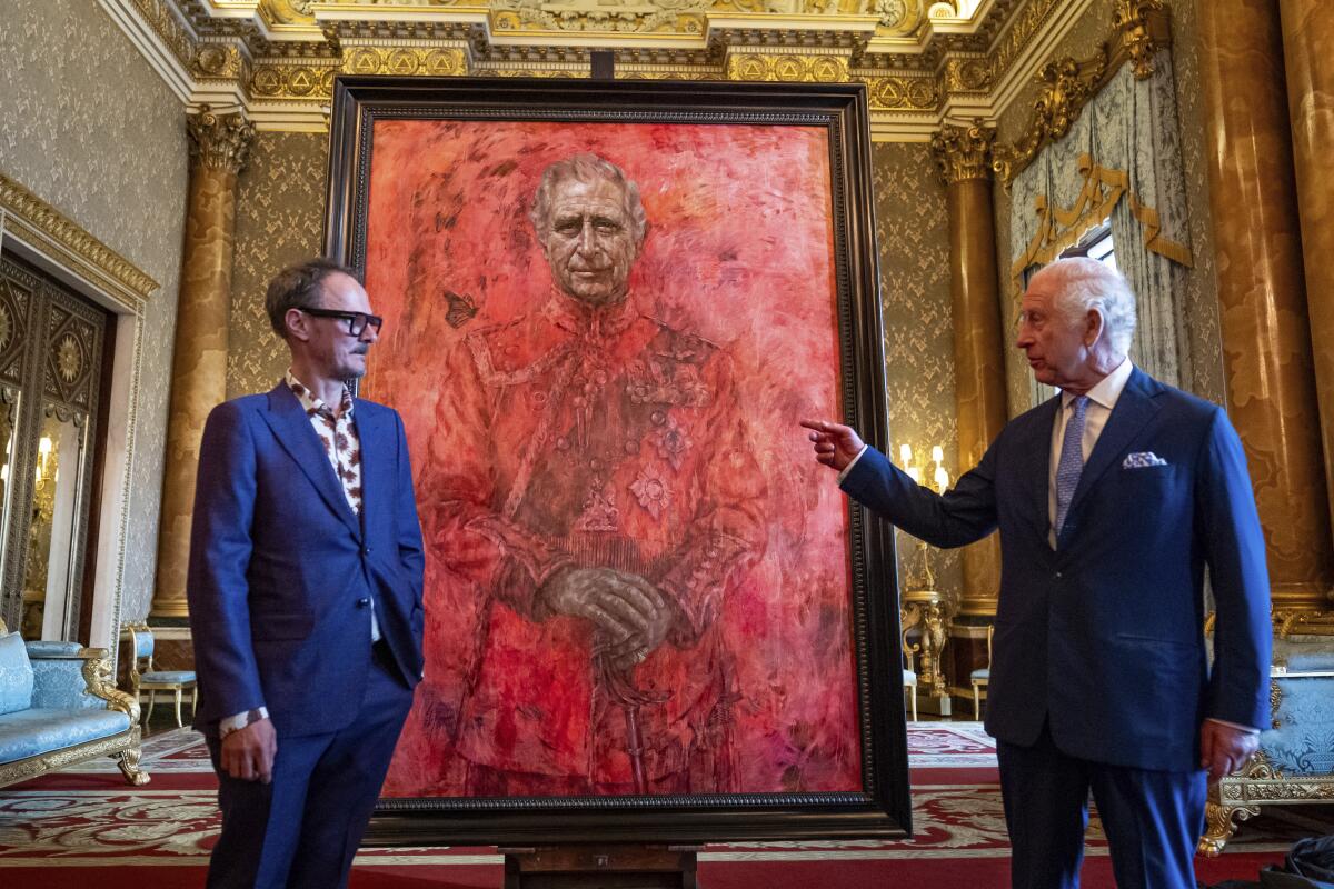 Artist Jonathan Yeo and King Charles III stand on either side of a portrait of the king in the red uniform of Welsh Guards