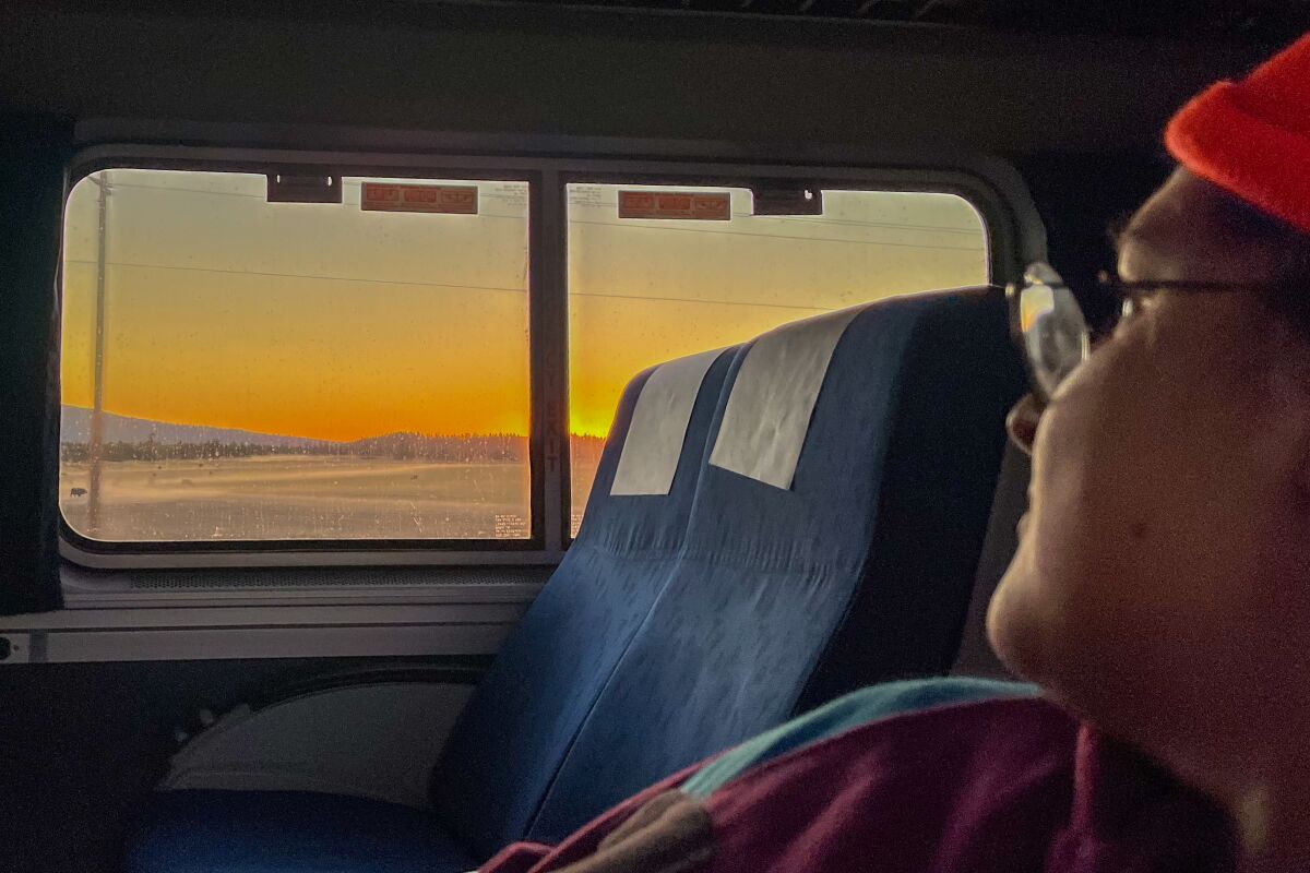 A view across the aisle of train, out the window to a sunset 