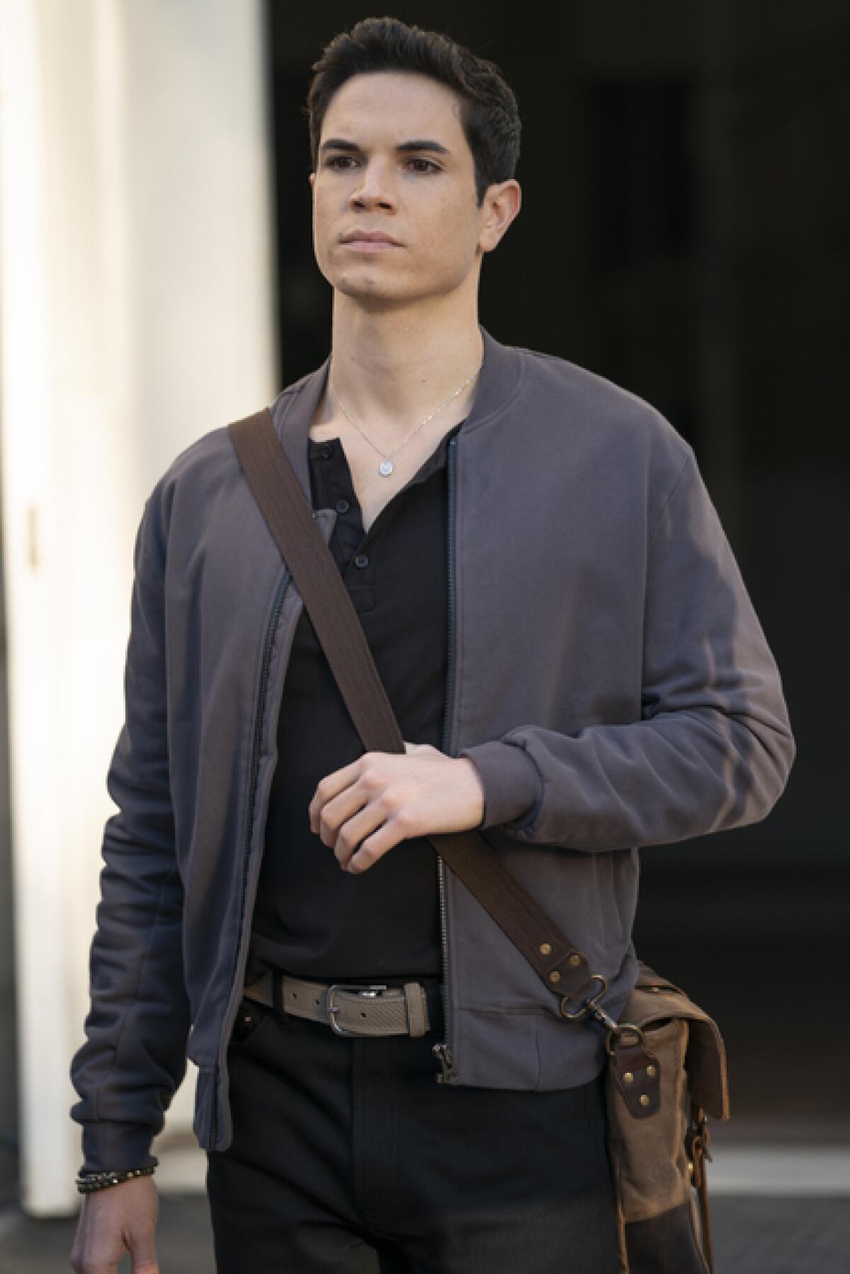 A man in a black shirt and a gray cardigan with a leather bag slung over his shoulder