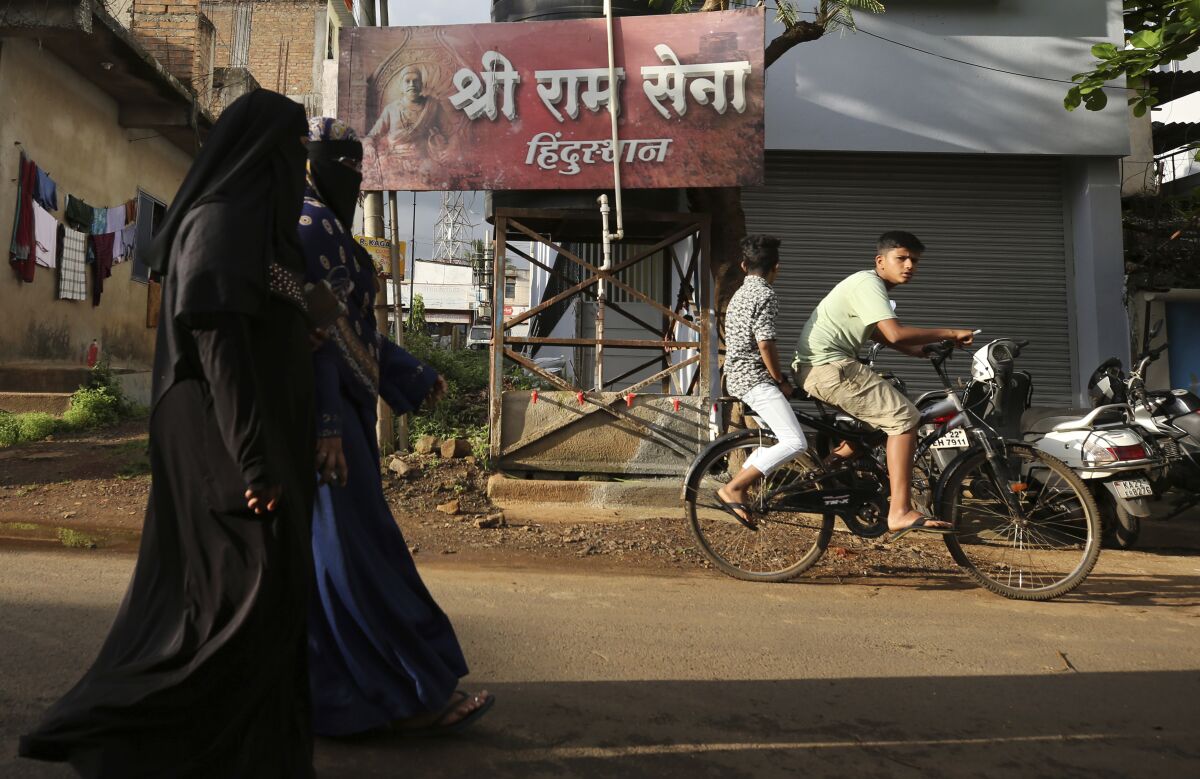 FILE- Unidentified Muslim women walk past a board displaying the name of the Hindu nationalist group Sri Ram Sena Hindustan in a residential neighborhood in Belagavi, India, Oct. 7, 2021. Police elsewhere in India have arrested a man alleged to be behind the offering for sale of prominent Muslim women through a fake online auction, in a case that has sparked anger and outrage across the country. (AP Photo/Aijaz Rahi, File)
