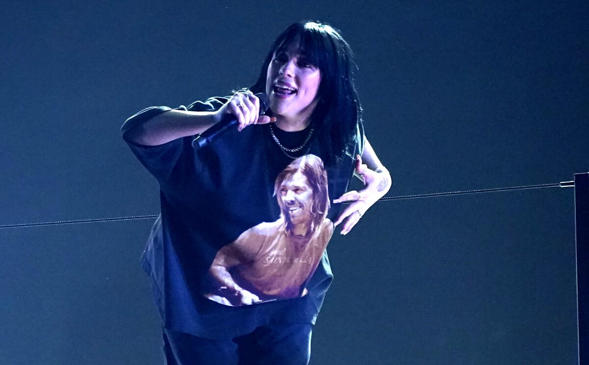 A woman with black hair wears a T-shirt as she sings