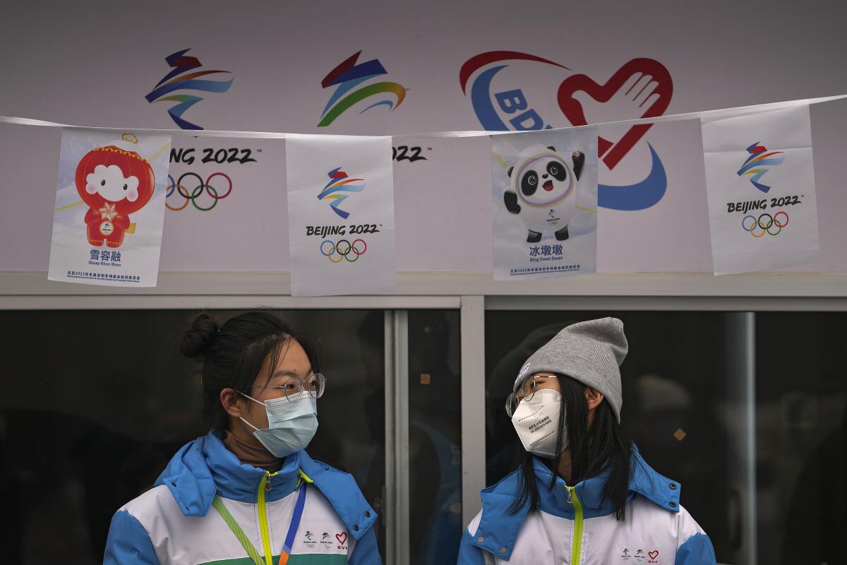 Volunteers wearing face masks to help protect from the coronavirus chat with each other at an information booth for the Beijing Winter Olympics Games at Qianmen Street, a popular tourist spot in Beijing, Sunday, Jan. 23, 2022. Chinese authorities have called on the public to stay where they are during the Lunar New Year instead of traveling to their hometowns for the year's most important family holiday. (AP Photo/Andy Wong)