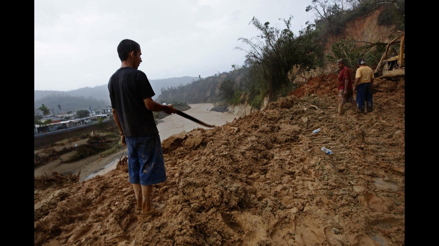 As the river rages through Utuado, citizens try to clear a road completely blocked by a mudslide cutting off people who live beyond.