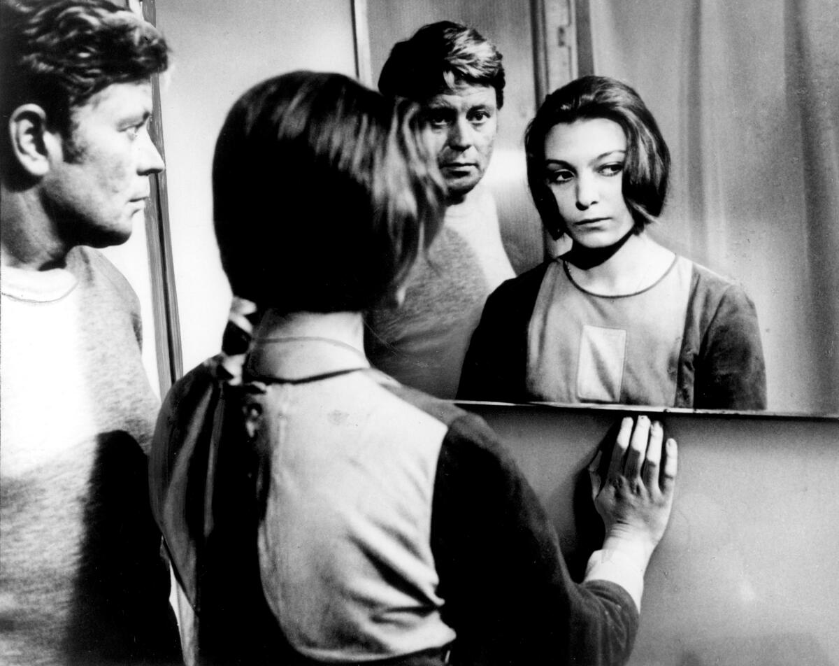 A man and a woman in futuristic clothing look in a mirror.