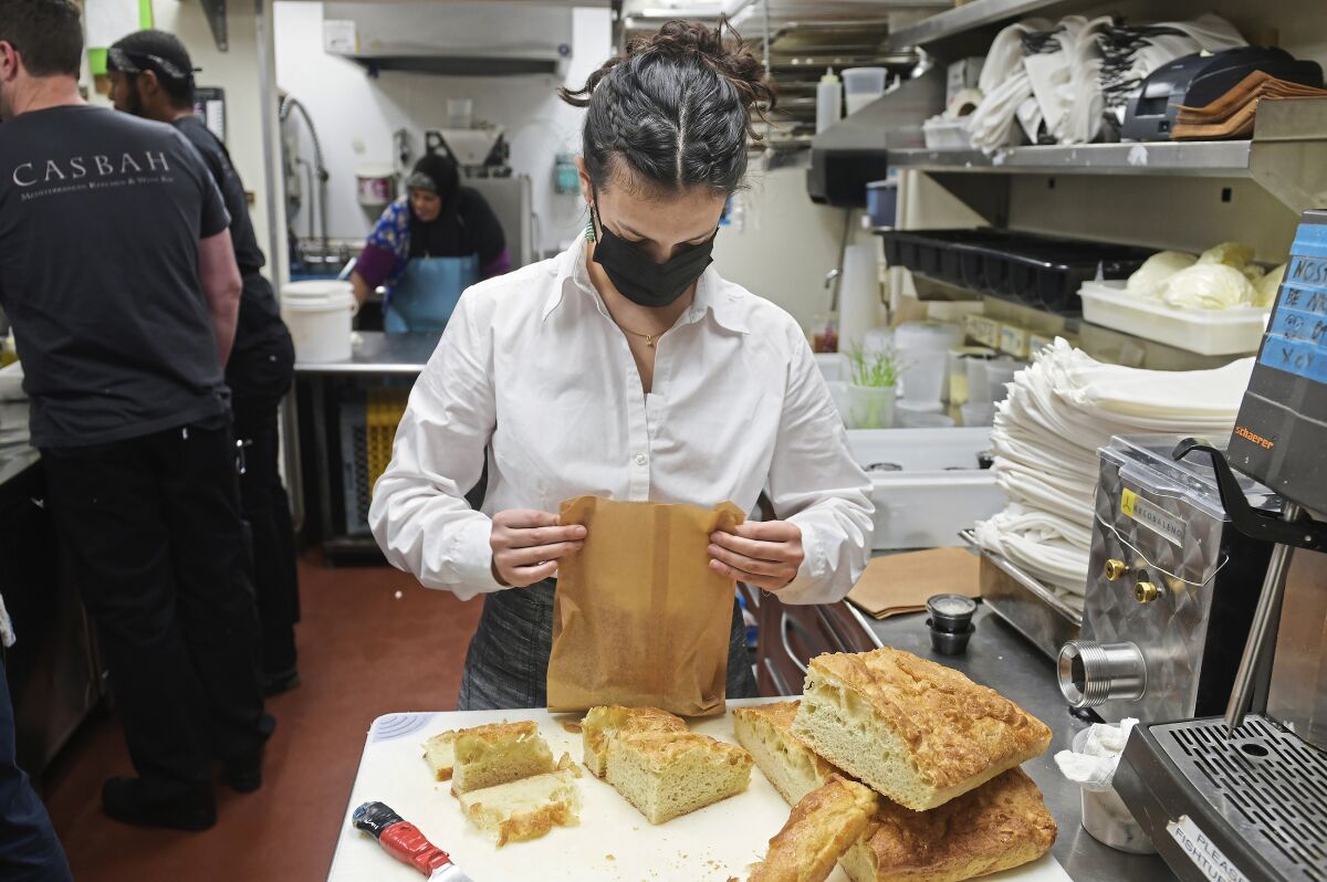 Hailey Shevitz, an employee at Casbah, cuts bread for take-out orders at the restaurant, Wednesday, Dec. 22, 2021, in Shadyside neighborhood in Pittsburgh. (Nate Guidry/Pittsburgh Post-Gazette via AP)