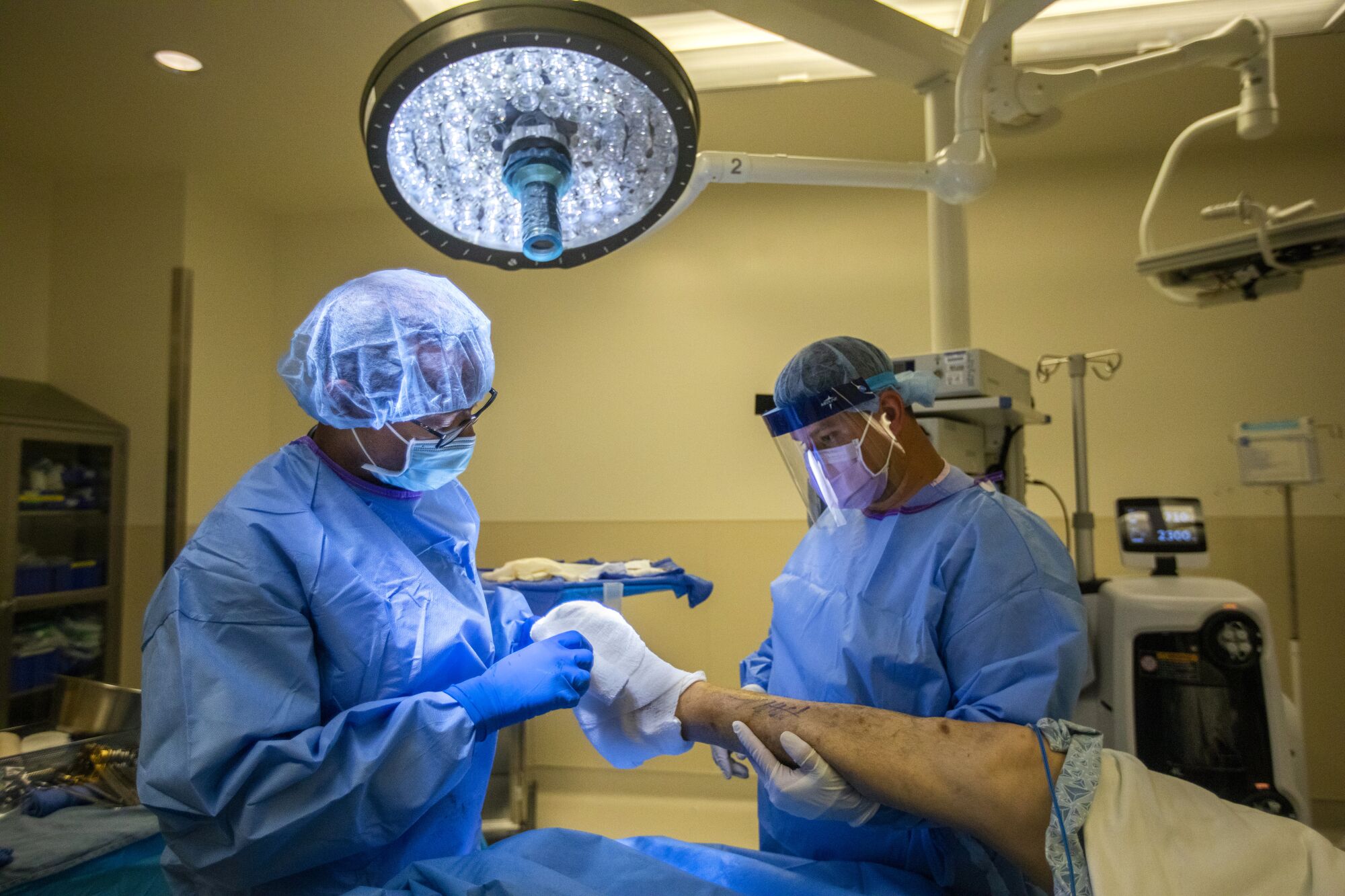 Dr. Myron Hall, left, and Ali Yousufzad, a surgical assistant, right, bandage Tony Zamora's foot after the surgery.