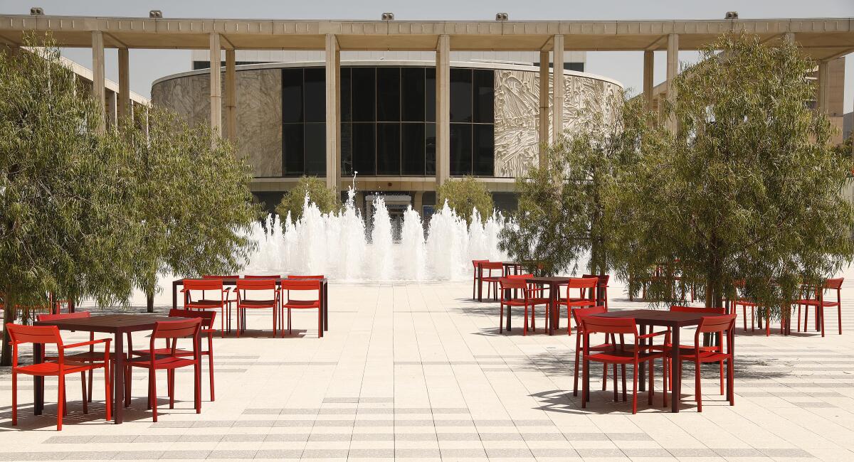 Chairs and tables on a plaza in front of a fountain with the Mark Taper Forum in the background. 