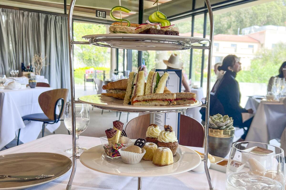Tower of sandwiches and desserts on a table in a covered outdoor dining space