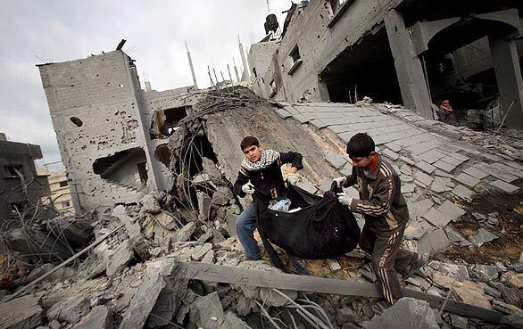 Two Palestinian brothers carry some of their clothes out of the rubble of their house, which was destroyed in an Israeli missile strike on the house of senior Hamas leader Nizar Rayan in the refugee camp of Jabaliya in northern Gaza.