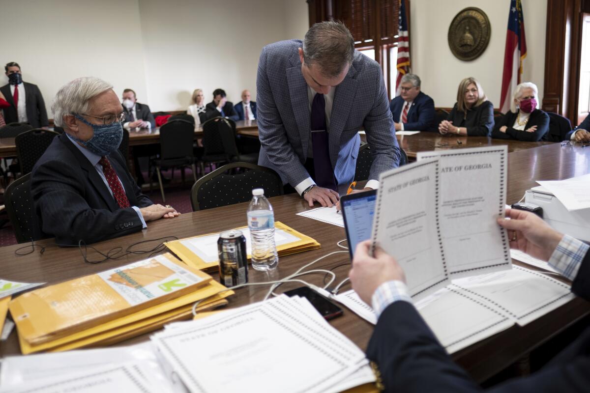 A man leans over a table where other people sit with paperwork. 