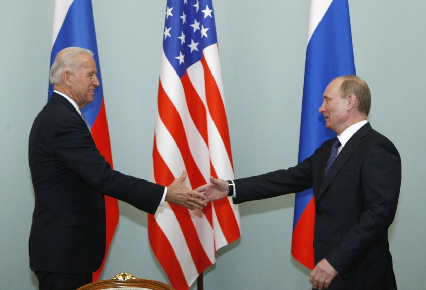 Biden and Putin, backed by Russian and U.S. flags, reach out to shake hands.