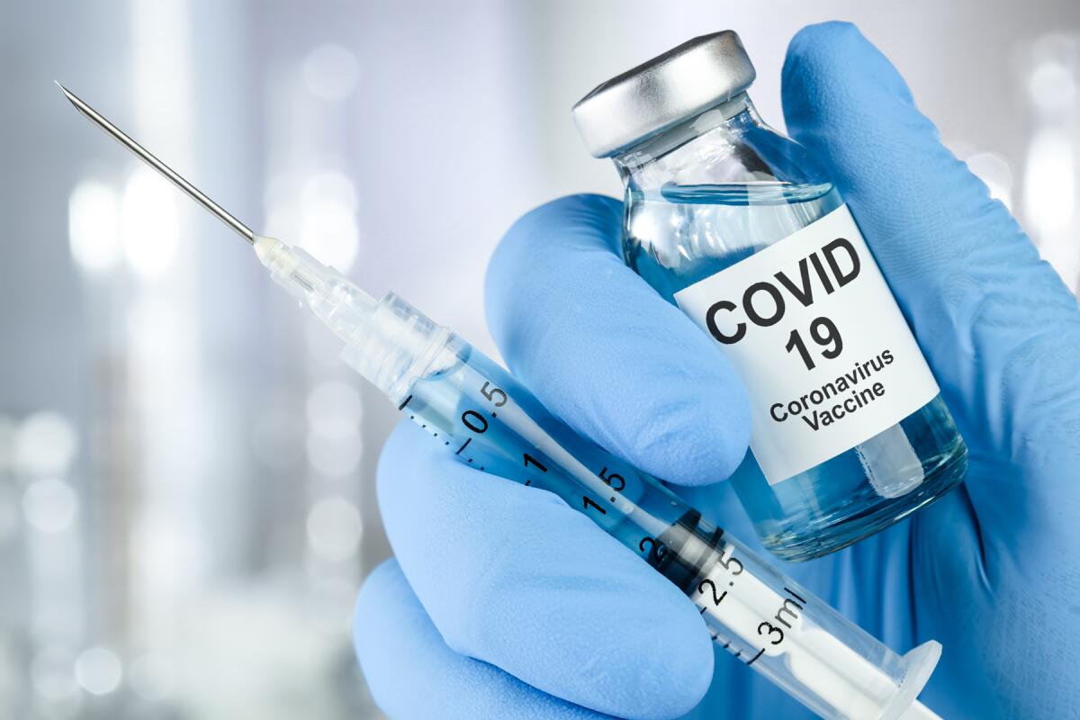 A person holds up a vial of COVID-19 vaccine and a syringe.