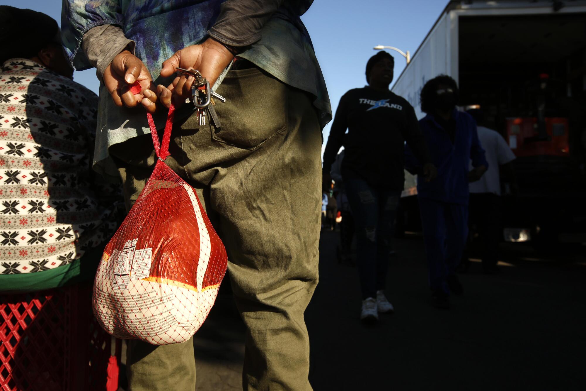 A wrapped turkey hangs from hands behind a person outdoors.