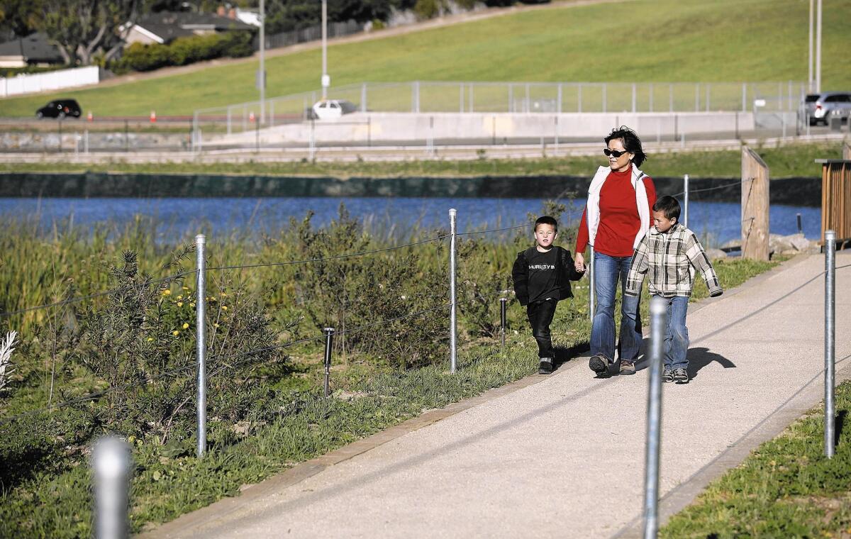 Visitors to Costa Mesa’s Fairview Park walk along a path in the park’s artificial wetlands. The city unveiled a strategy this week to deal with mosquitoes breeding in that area.