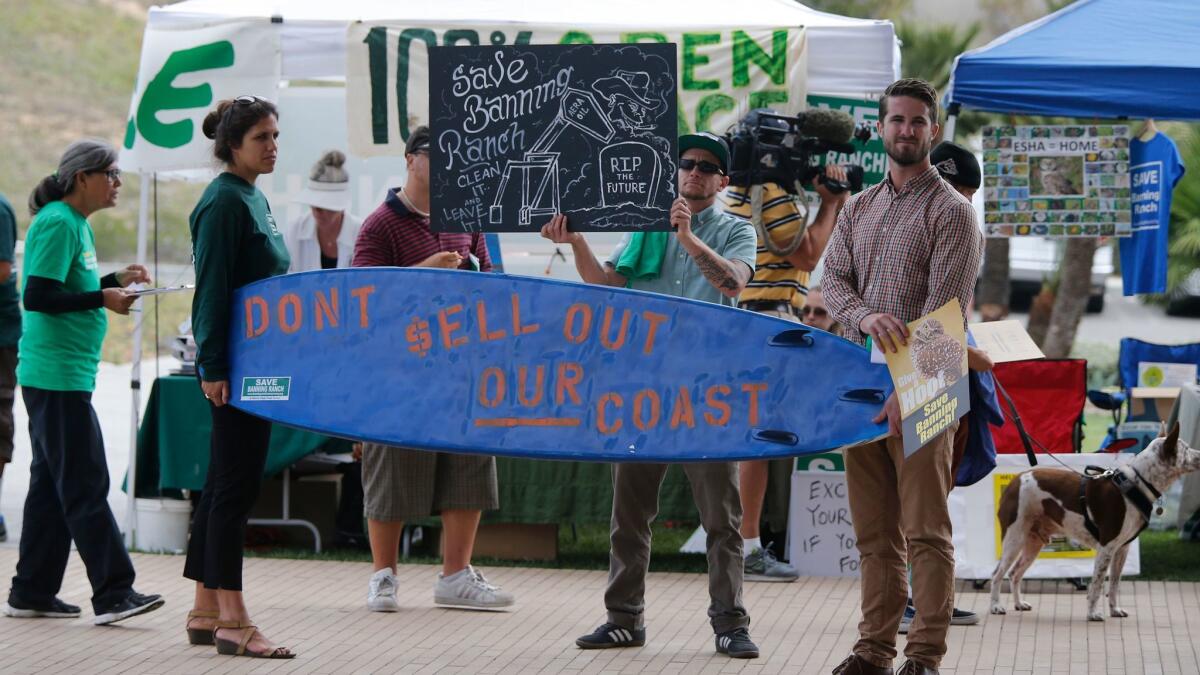 Arlis Reynolds, left, and Rob Moddelmog hold a surfboard while Cody Parole holds a sign against the development of Banning Ranch during the California Coastal Commission hearing in Newport Beach on Sept. 7, 2016.