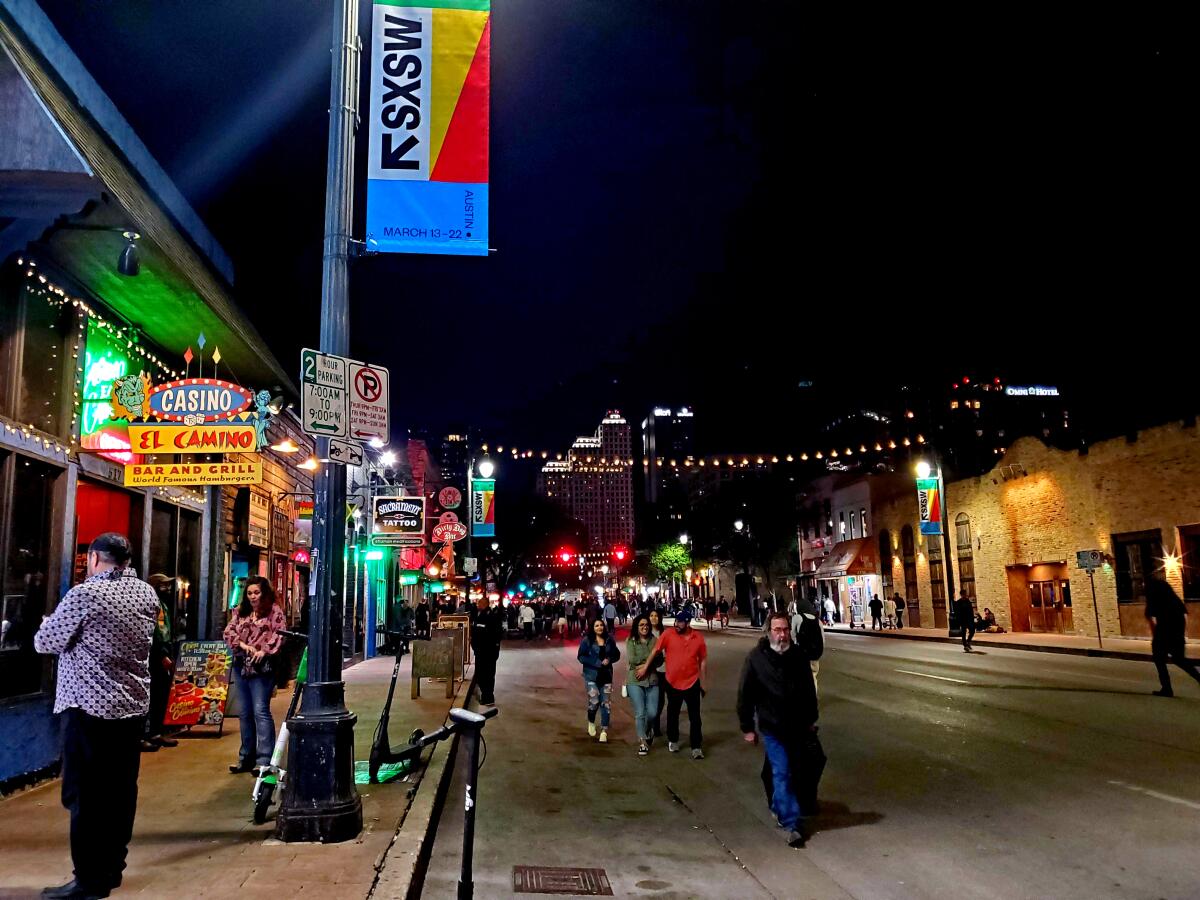 People walking down a lit street at night. 