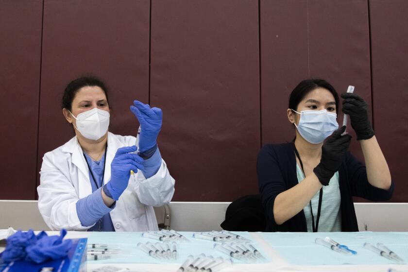 Pharmacists Nabilah Seblini and Julie Nguyen prepare syringes with the COVID-19 vaccine made by Johnson & Johnson at a high school in Detroit.