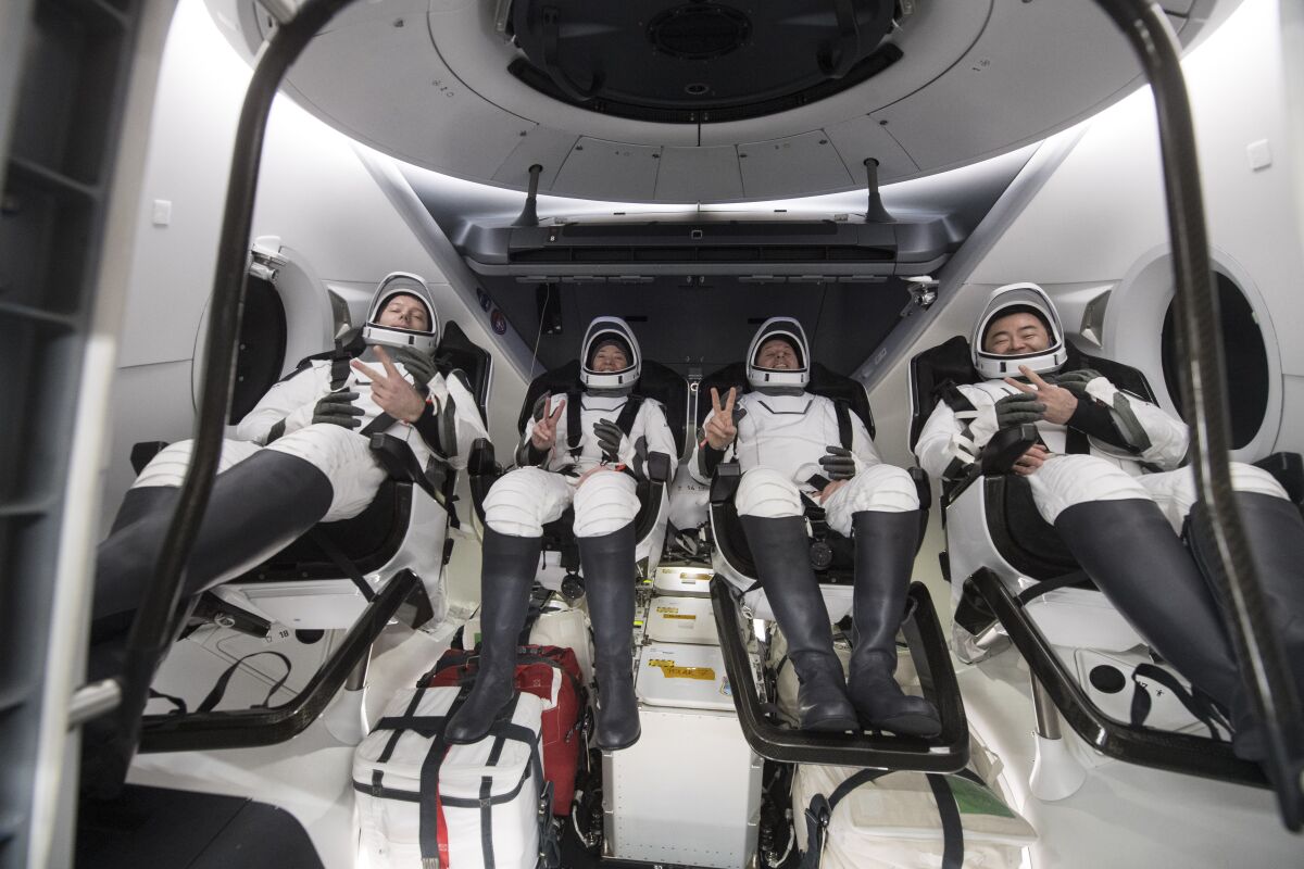 Four astronauts gesture inside a spacecraft.
