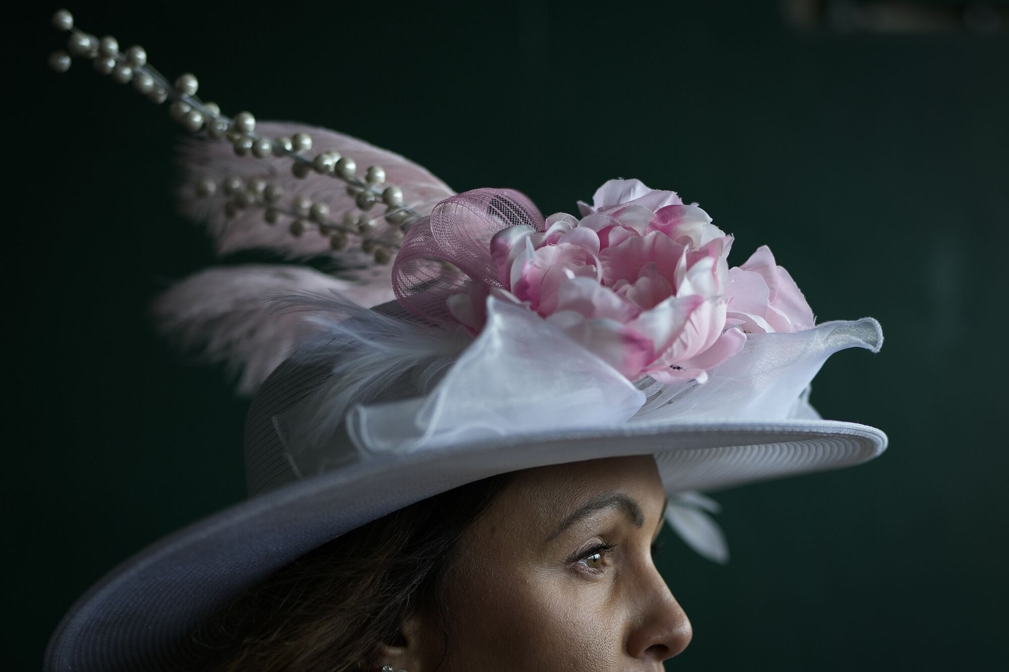 A woman wearing a white and pink hat walks to her seat at Churchill Downs. 