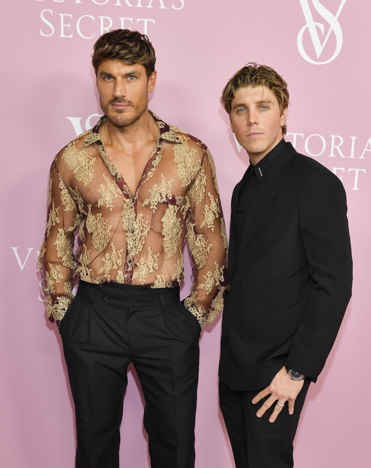 Chris Appleton is wearing a sheer gold and black top and poses alongside Lukas Gage in a black shirt and pants