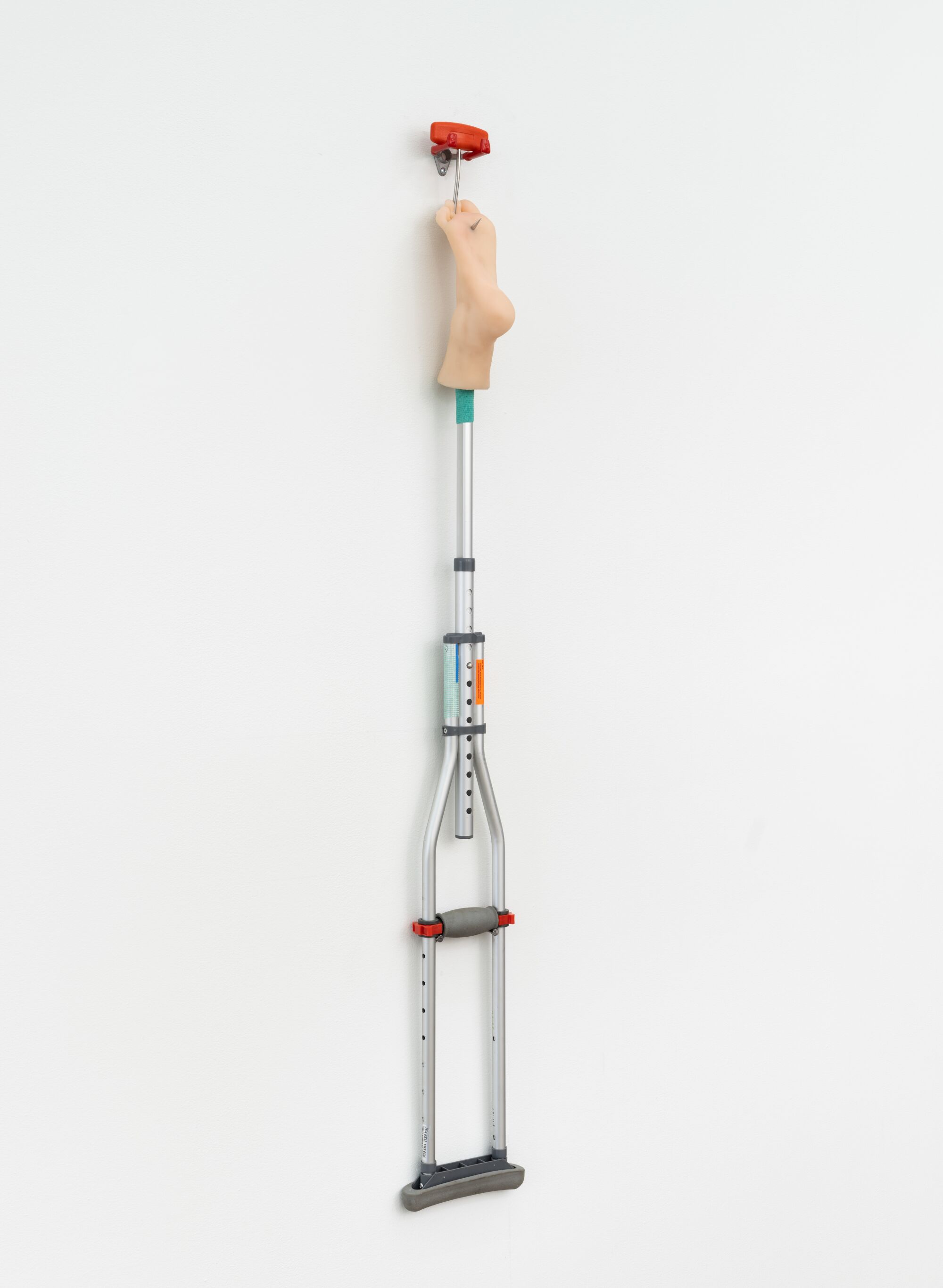 An artwork by Abareshi of a crutch on the wall with a plastic foot at the end.