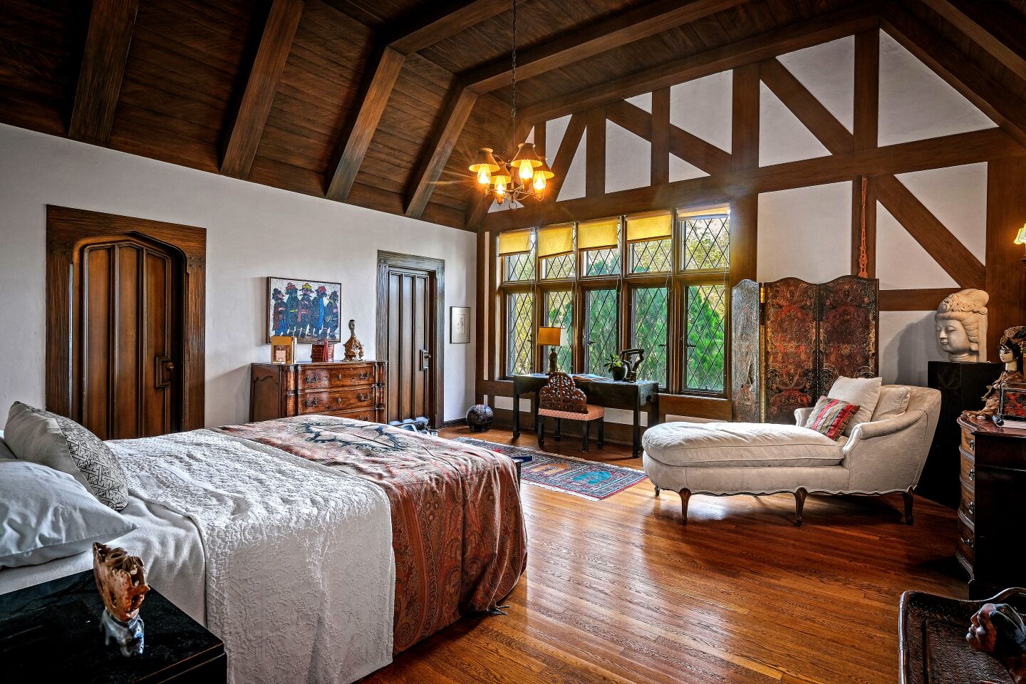 An upper-level bedroom with high wood-beamed ceilings and mullioned windows