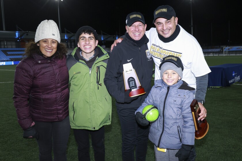 Coach Chris Chamides (with trophy), assistant Michael Erush and family celebrate winning the Division II soccer championship.