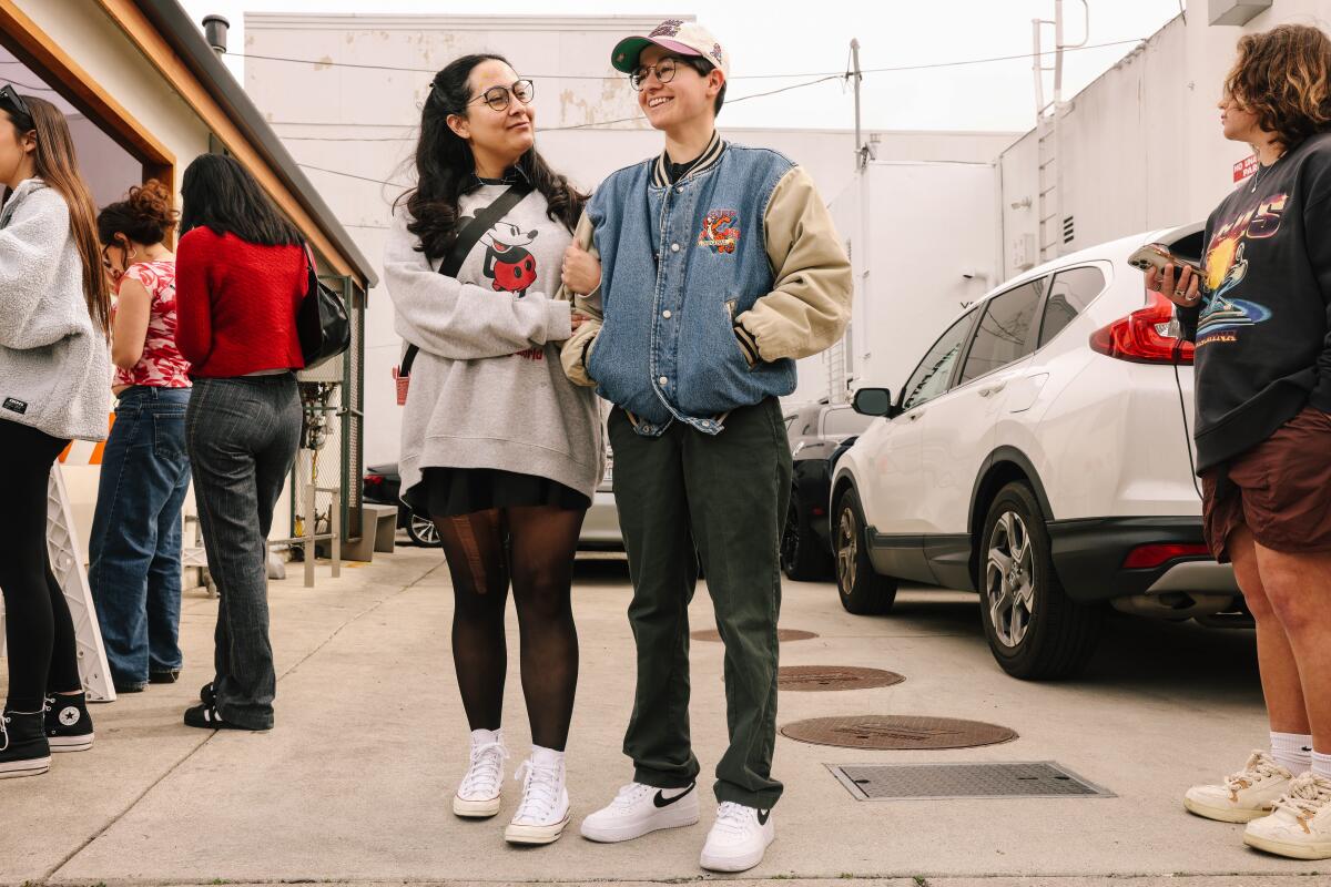 People in line outside a store include a pair posing arm in arm for a portrait