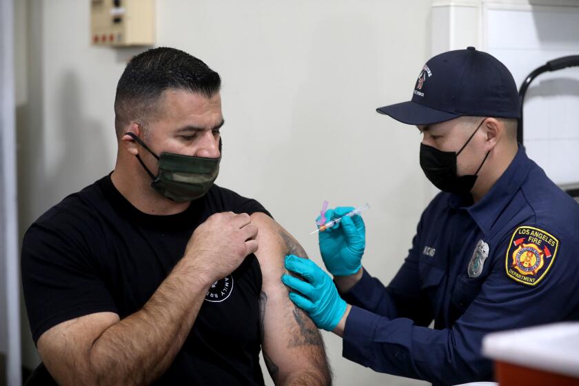 LOS ANGELES, CA - DECEMBER 28: Elliot Ibanez, left, Los Angeles Fire Department (LAFD) captain, receives a Moderna COVID-19 vaccination given by Anthony Kong, LAFD firefighter paramedic, at Station 4 on Monday, Dec. 28, 2020 in Los Angeles, CA. Mayor of Los Angeles Eric Garcetti and Ralph M. Terrazas, LAFD fire chief, were there to observe the rollout of the vaccination program. (Gary Coronado / Los Angeles Times)
