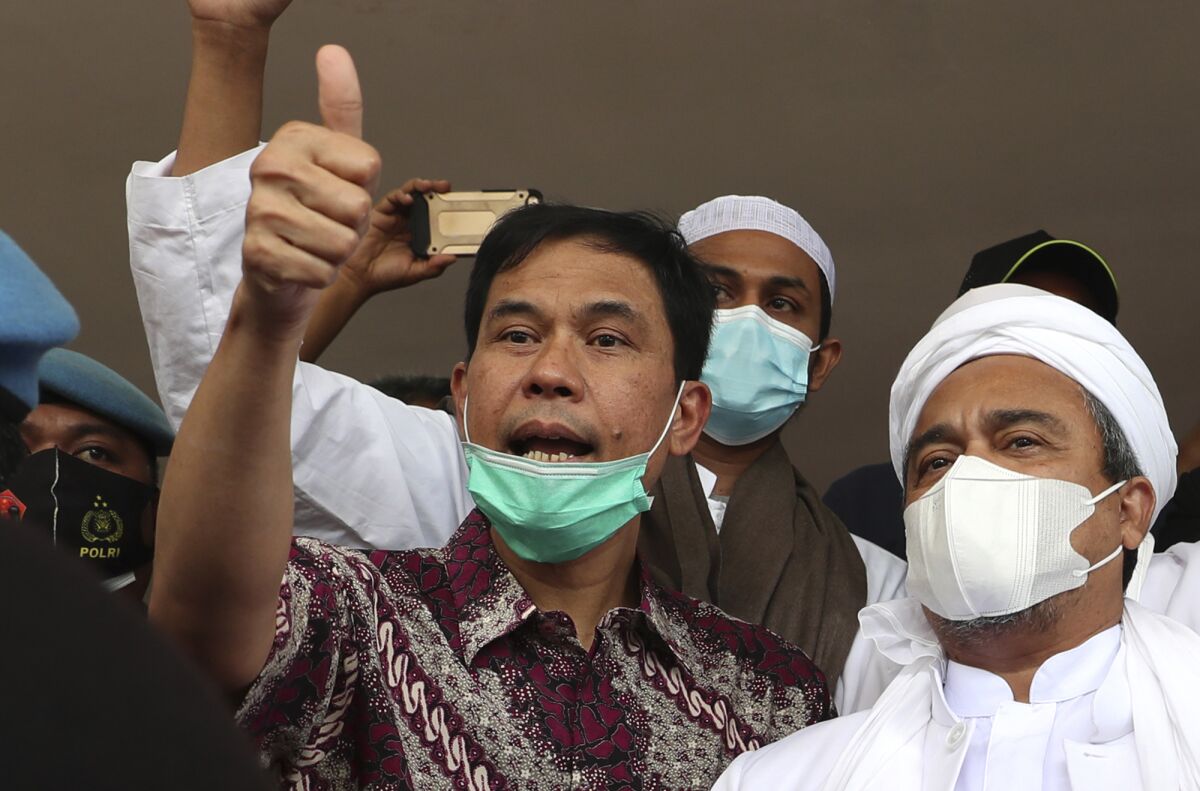 FILE - General secretary of the now-defunct Islam Defenders Front Munarman, left, who is also the lawyer of firebrand cleric Rizieq Shihab, right, gestures at reporters after Rizieq's questioning at the Regional Police Headquarters in Jakarta, Indonesia on Dec. 12, 2020. The former human rights lawyer was sentenced to three years in prison on Wednesday, April 6, 2022 after an Indonesian court found him guilty of inciting people to carry out radicalism with aim to change the country's secular government to the Islamic caliphate. (AP Photo/Achmad Ibrahim, File)