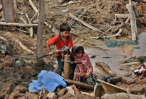 Young Pakistani flood survivors wash their clothes at a pump in the rubble in Nowshera.