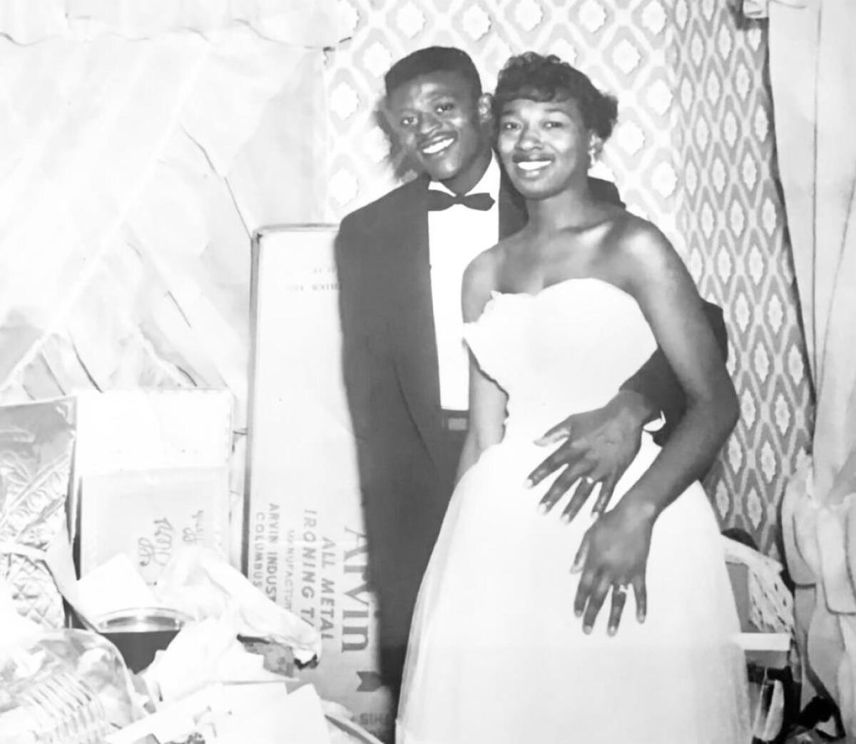 A man in a tuxedo and a woman in a wedding dress smile next to each other.