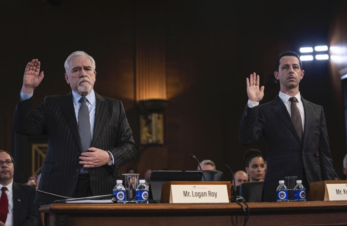 Two men in dark suits raise a hand to take an oath.